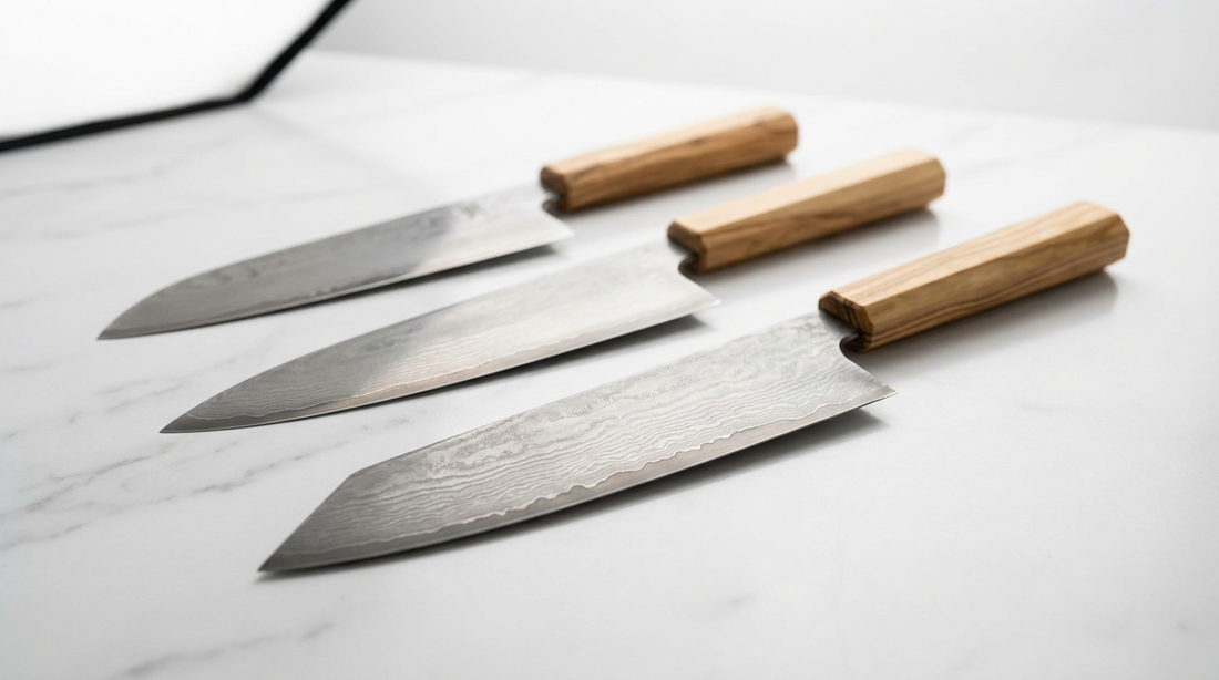 Trois couteaux de chef en acier damas avec manches en bois d'olivier, alignés sur un plan de travail en marbre blanc