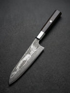 Couteau Santoku 18 cm en acier Damas AUS-10 avec manche en bois noir sur fond gris texturé