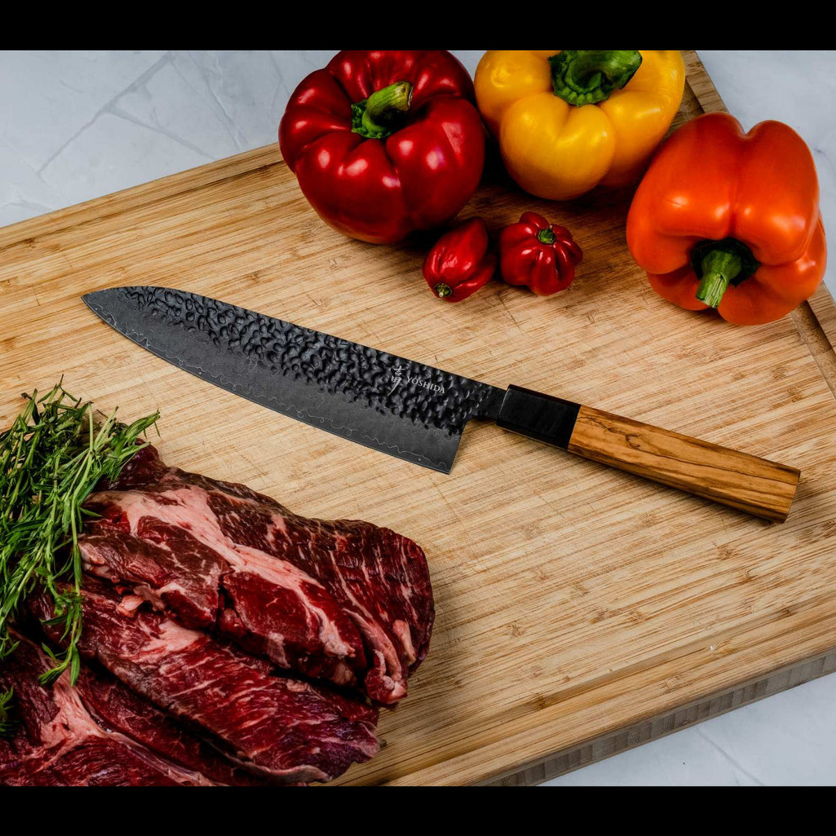 Gyuto 20 cm à manche en olivier sur une planche, avec poivrons, herbes et viande, vendu en set avec le Santoku 17 cm
